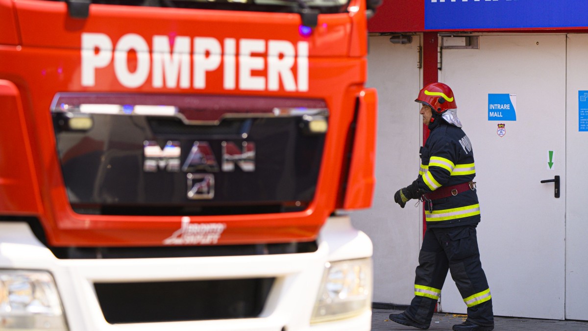 Un pompier echipat pentru intervenție intră într-o clădire, lângă o autospecială.