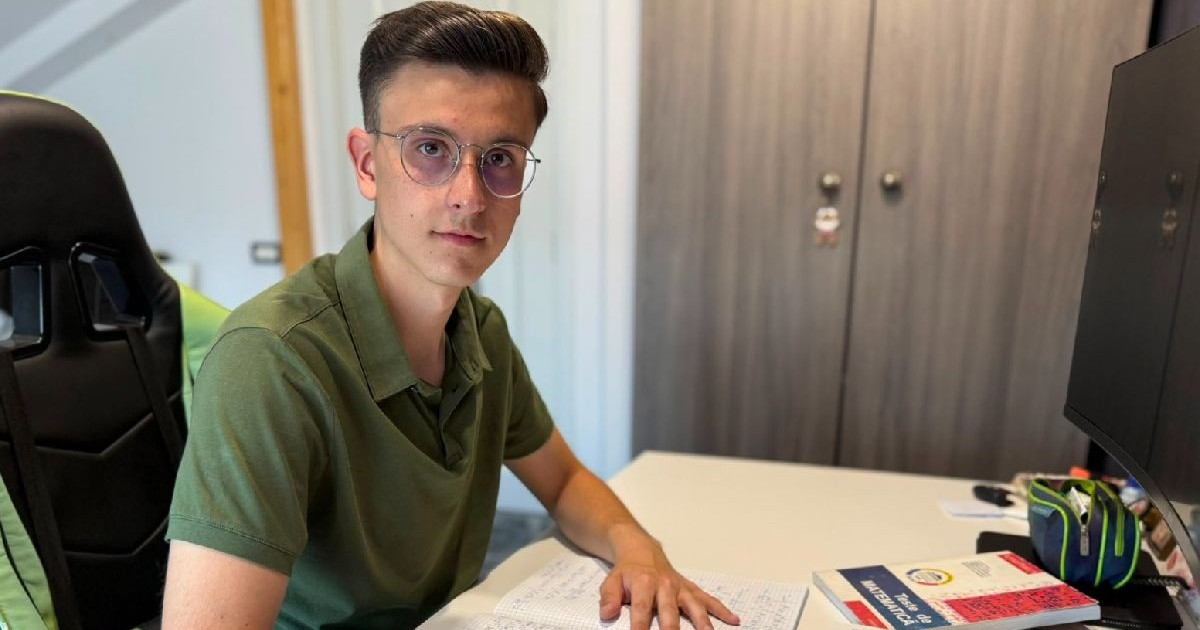 Un elev cu ochelari si tricou verde sta la un birou si lucreaza la matematică