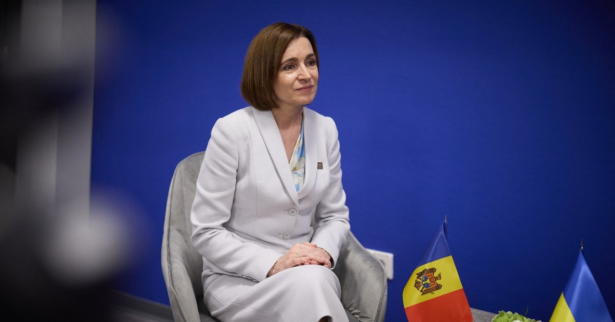 Maia Sandu îmbracată într-un compleu gri pe fundal albastru, alături de un steguleț al Republicii Moldova așezat pe un birou în dreapta președintei