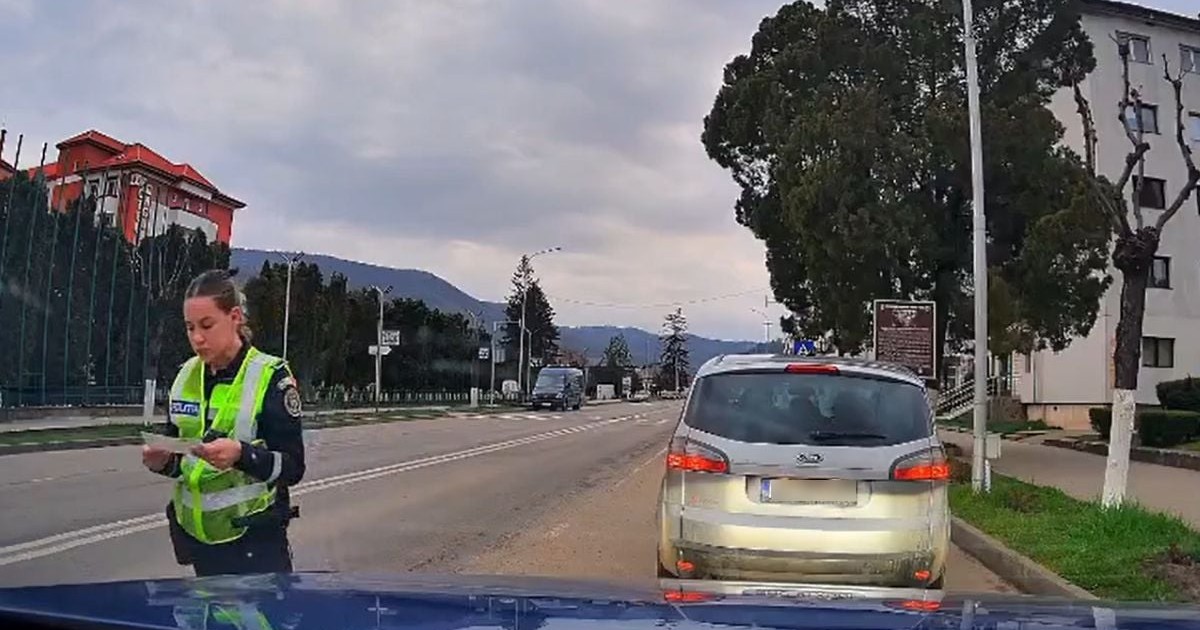 Polițistă îmbrăcată în uniformă, pe o stradă din Târgu Ocna, cu o mașină parcată în lateral, de culoare gri