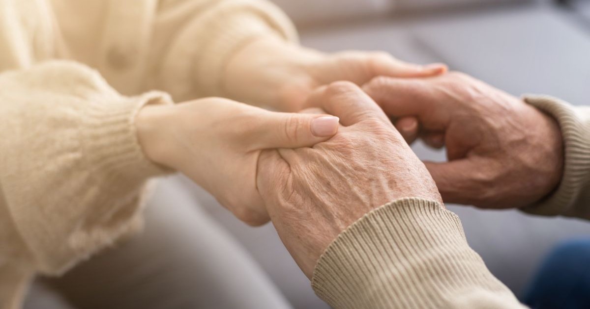 Mâinile unui pensionar în vârstă sunt ținute în mâini de o tânără fizioterapeut grijulie.