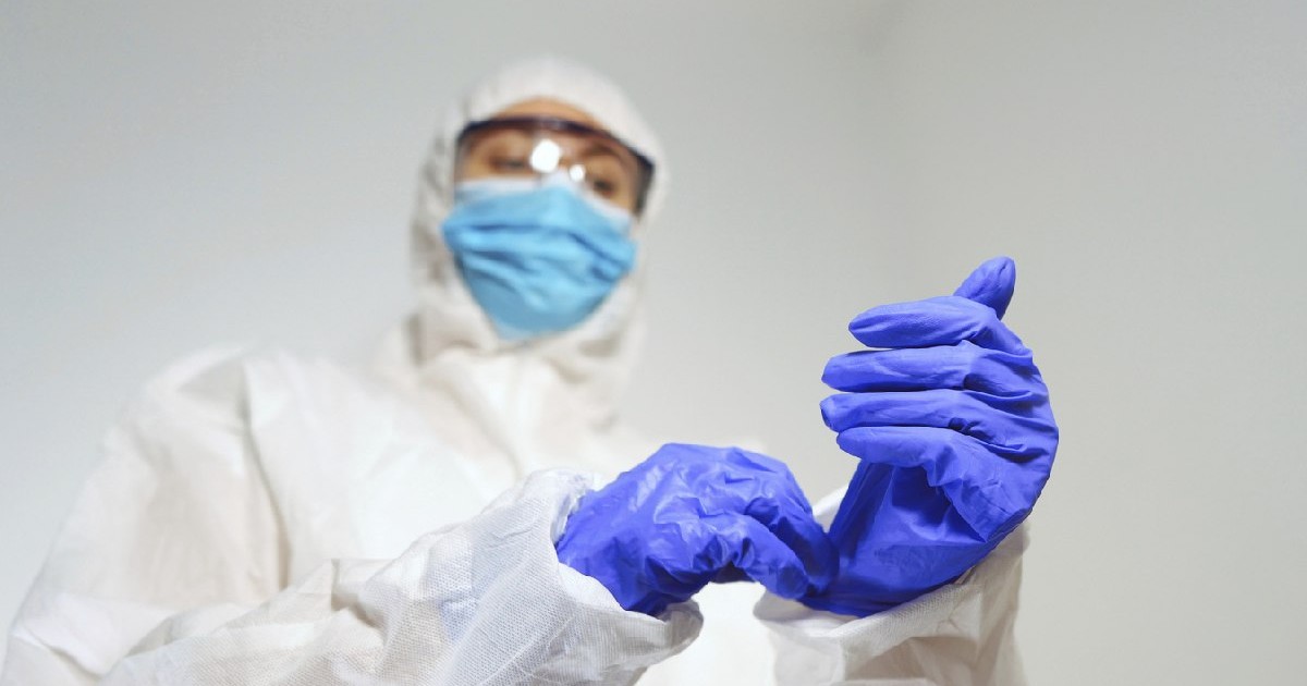 Personal medical în costum de protecție își pune mănușile