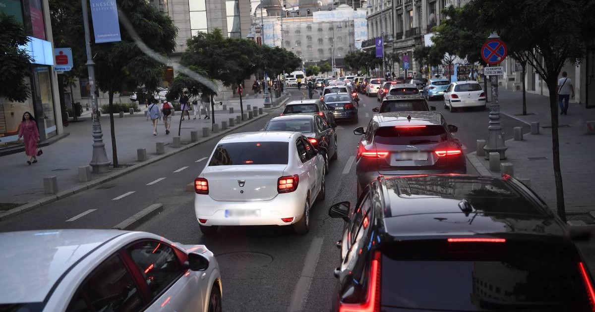 Trafic intens pe Calea Victoriei din centrul Bucureștiului. Se pot observa mai multe mașini în mișcare lentă. Pe partea stângă a imaginii se află trotuarul cu trecători, stâlpi ornamentali și indicatoare rutiere.