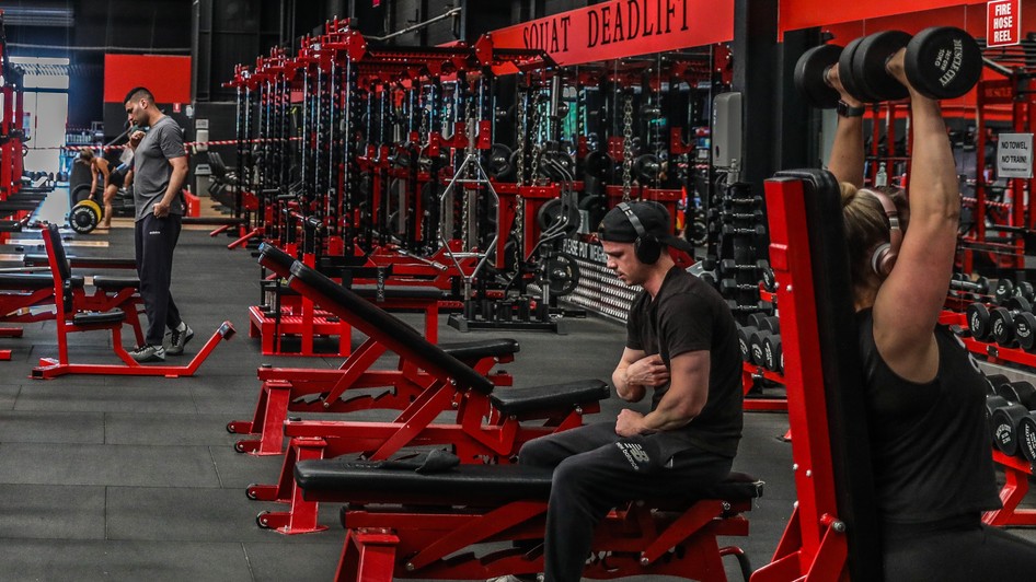 Imagine dintr-o sală de fitness, cu mai mulți oameni antrenându-se la diverse aparate