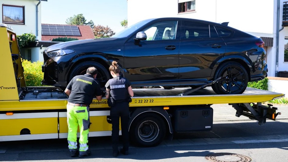 Un autoturism BMW negru încărcat pe platforma unei mașini de tractare, în timp ce un operator și o femeie agent fixează vehiculul.
