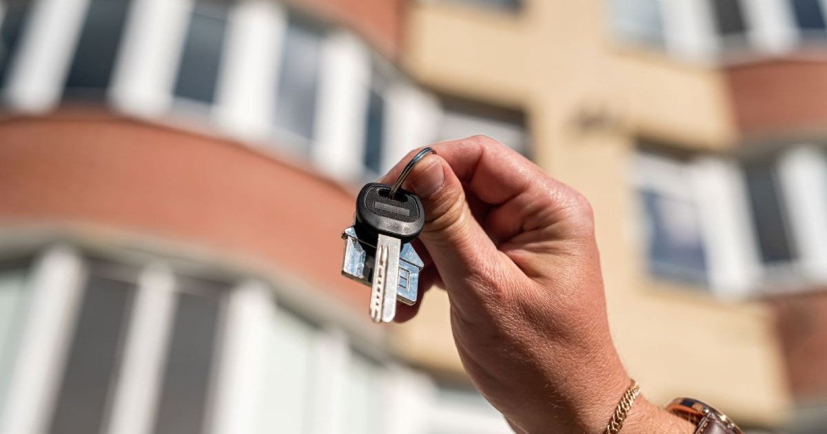 Un set de chei este ținut în mână fața unui bloc de apartamente