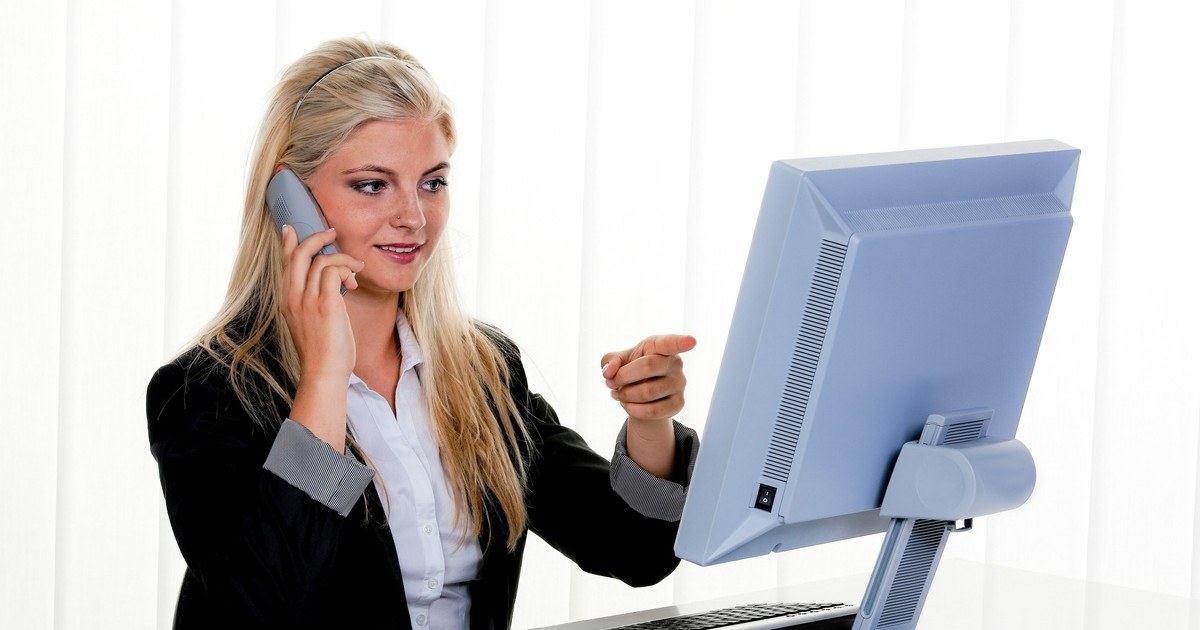 O femeie vorbește la telefon și arată cu degetul către monitor, într-un call center.