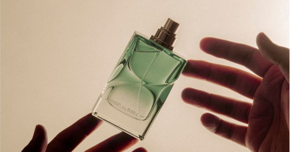 Sticla de parfum verde tinuta intre degetele de la ambele maini