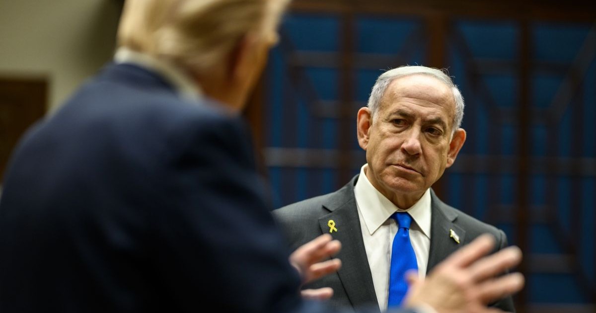 Benjamin Netanyahu, în fundal, îmbrăcat în costum negru, cămașă albă și cravată albastră, iar în prim plan, în blur și cu spatele, Donald Trump