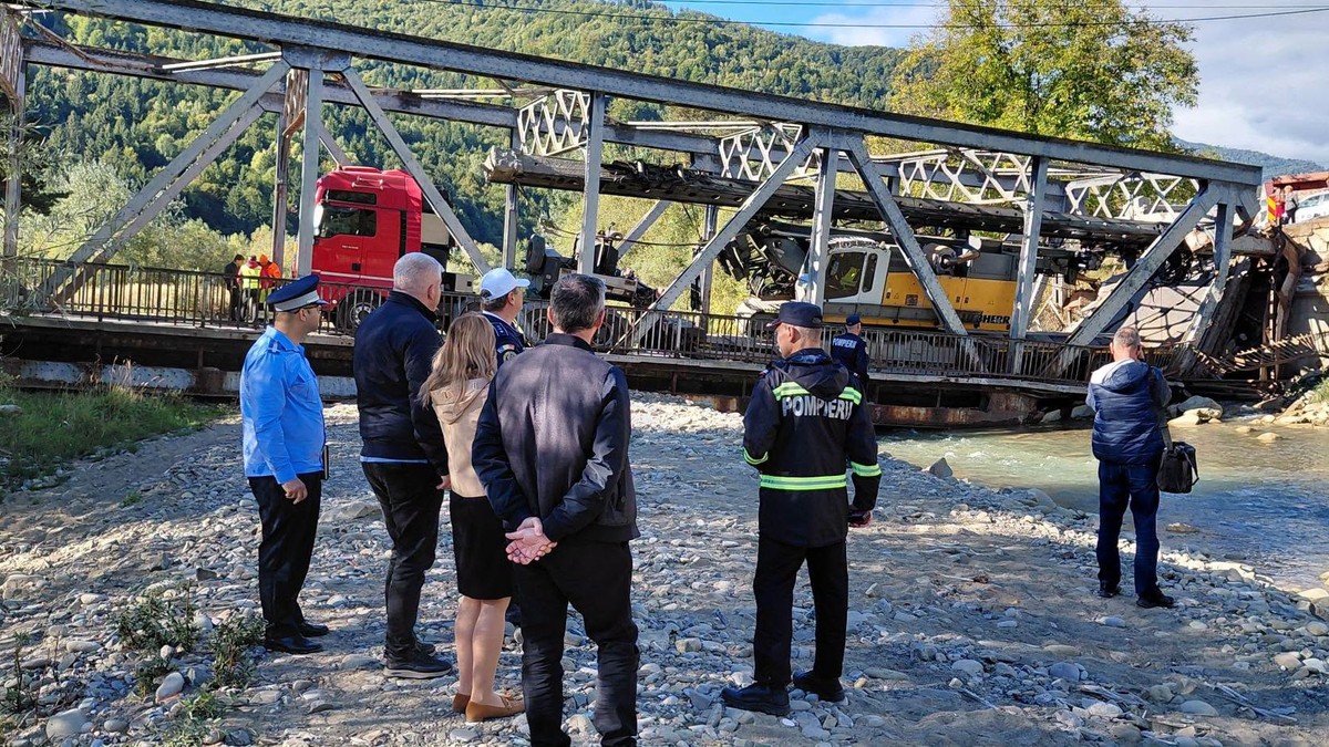 Mai multe persoane privesc la un pod metalic care a fost distrus de greutatea unui camion care transporta o macara