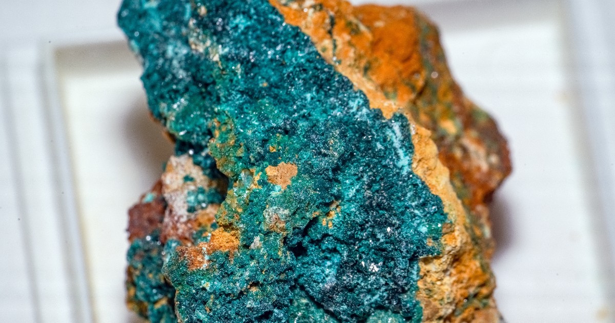 Imaginea prezintă un specimen de herbertsmithită, un mineral de culoare verde-albăstruie, expus pe o matrice de rocă maronie.