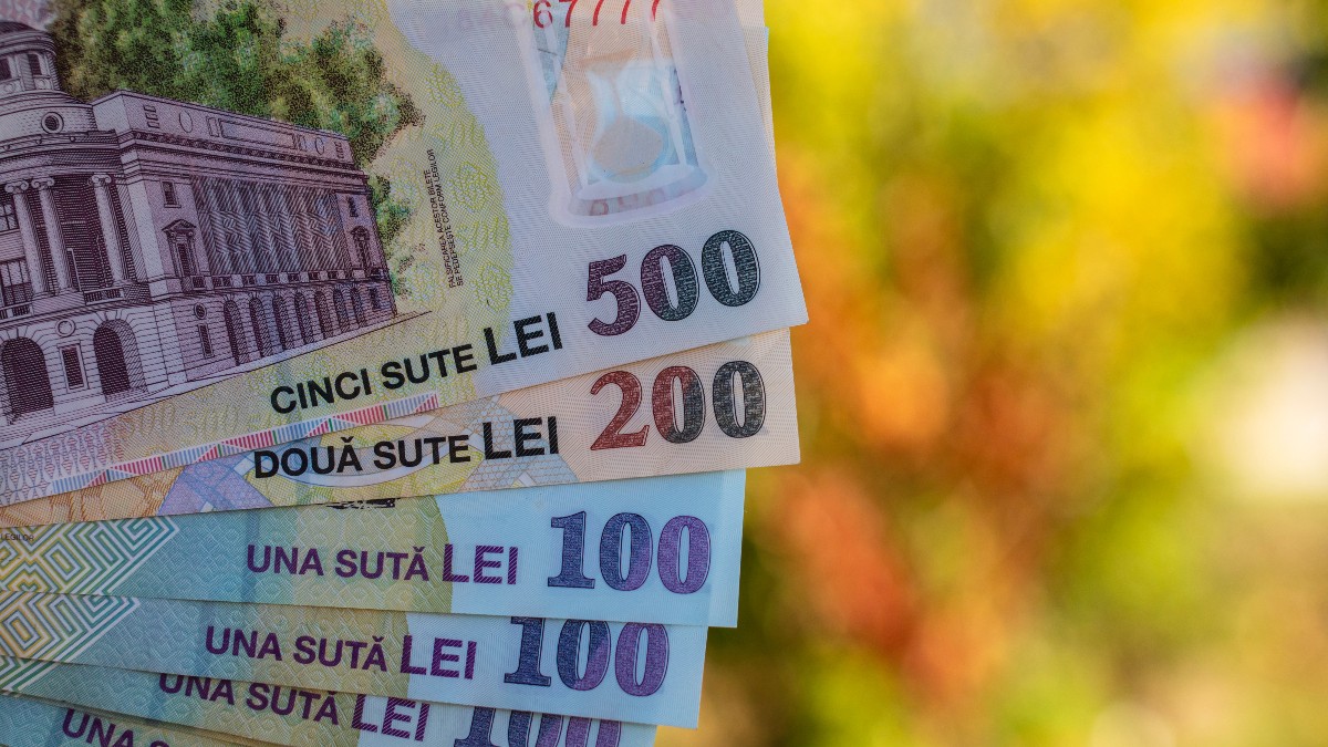 Imaginea prezintă mai multe bancnote românești de diferite valori (500, 200, 100 și 50 de lei), aranjate în evantai, cu un fundal colorat, neclar