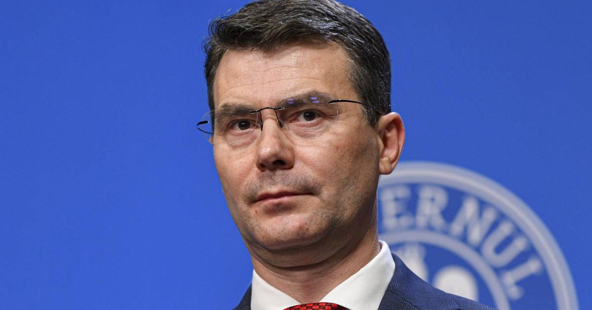 Horațiu Moldovan, șeful CNAS, în timpul unei conferințe de presă, poartă un costum albastru și o cravată roșie.