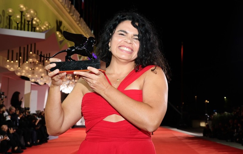 Regizoarea Alina Șerban, la Festivalul de Film de la Veneția, stă pe covorul roșu și ține în mână premiul
