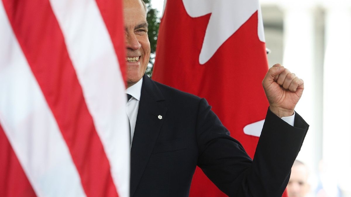Mark Carneu cu mâna stângă ridicată și pumnul strâns, între steagurile Americii și Canadei