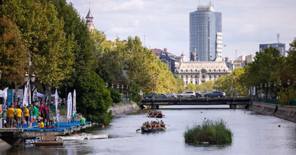 Râul Dâmbovița din București, cu două bărci în care se află oameni, iar pe fundal o clădire înaltă