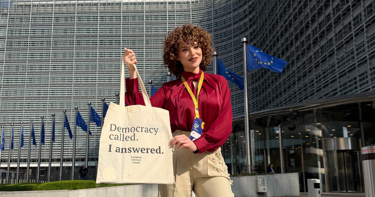 Ada Maria Ileana îmbrăcată într-o bluză grena și pantaloni crem arataă o sacosă pe care scrie: Democracy called. I answered. (Democratia m-a chemat. Eu am răspuns).