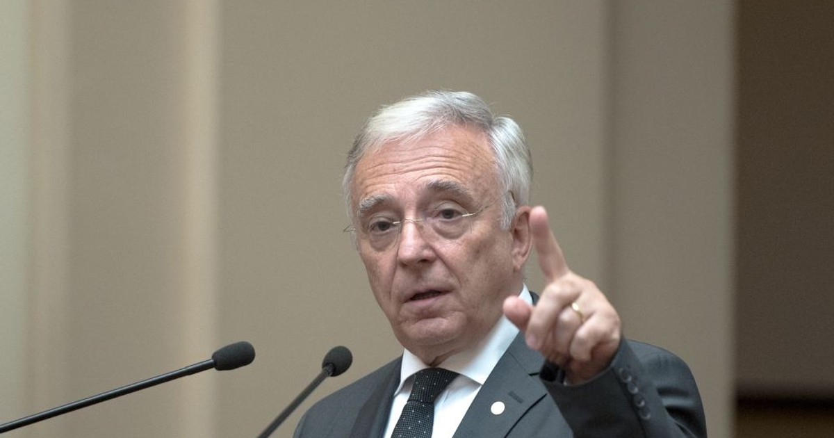 BNR prezintă raportul trimestrial asupra inflaţiei. Mugur Isărescu, la un pupitru, cu mâna stângă ridicată și degetul arătător în aer