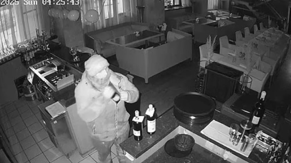 Imaginea surprinde un bărbat într-un restaurnat, filmat de o cameră de supraveghere, în timp ce bagă în haină o sticlă de vin