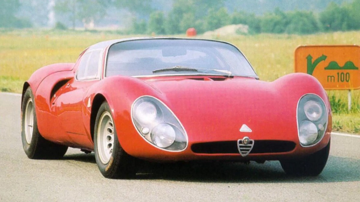 Un automobil sport clasic Alfa Romeo 33 Stradale, de culoare roșie, este fotografiat pe o pistă de testare sau pe un drum asfaltat.