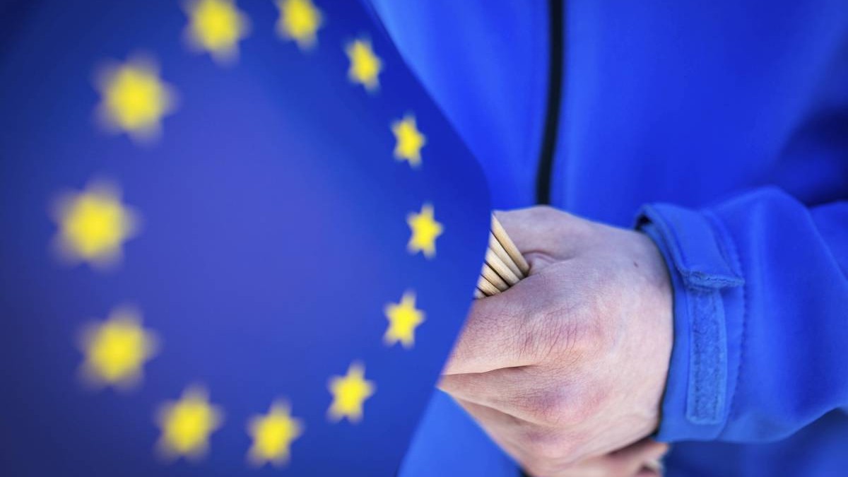 cadru strans maini care tin steaguru ale Uniunii europene, totul pe albastru
