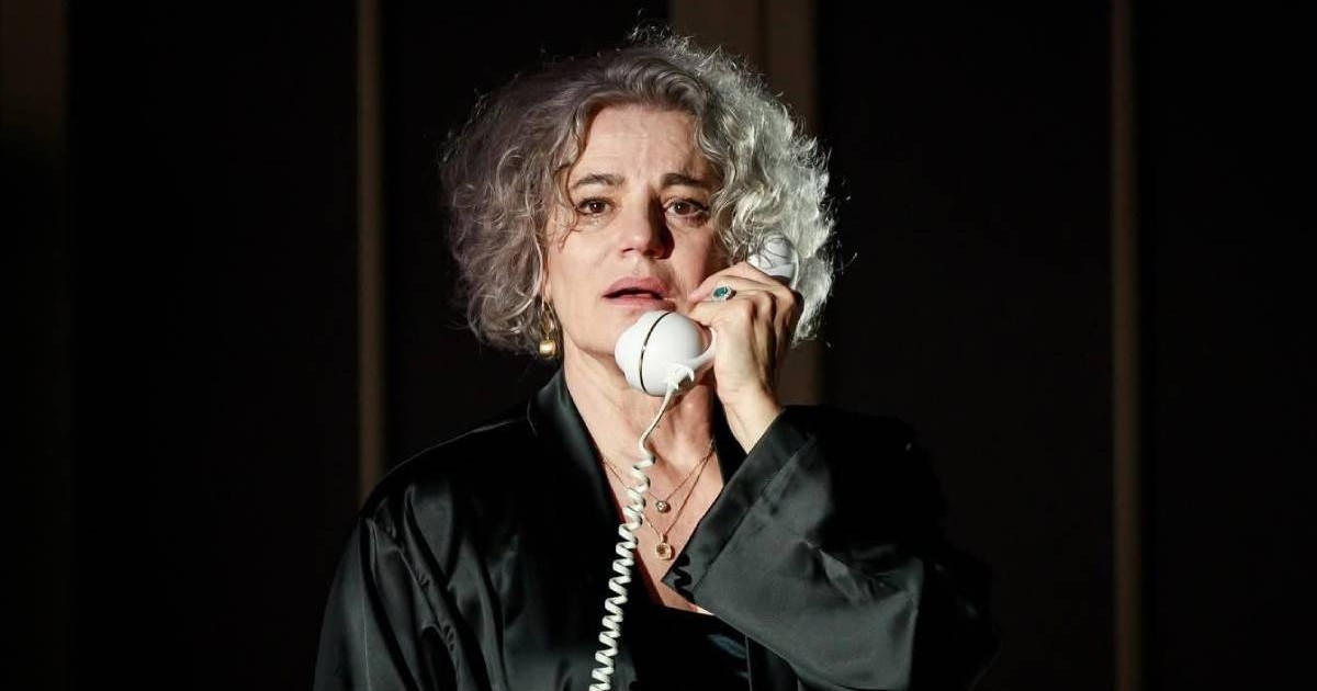 Maia Morgenstern, in constum negru, satinat, pe un fundal negru, cu receptorul unui telefon alb la ureche, in piesa