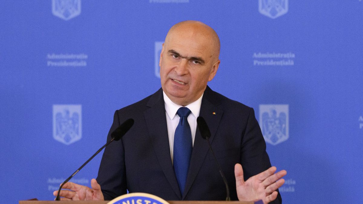 Ilie Bolojan, îmbrăcat la costum, ține mâinile larg deschise, în timp ce vorbește în cadrul unei conferințe de pesă la Palatul Cotroceni, mai 2025