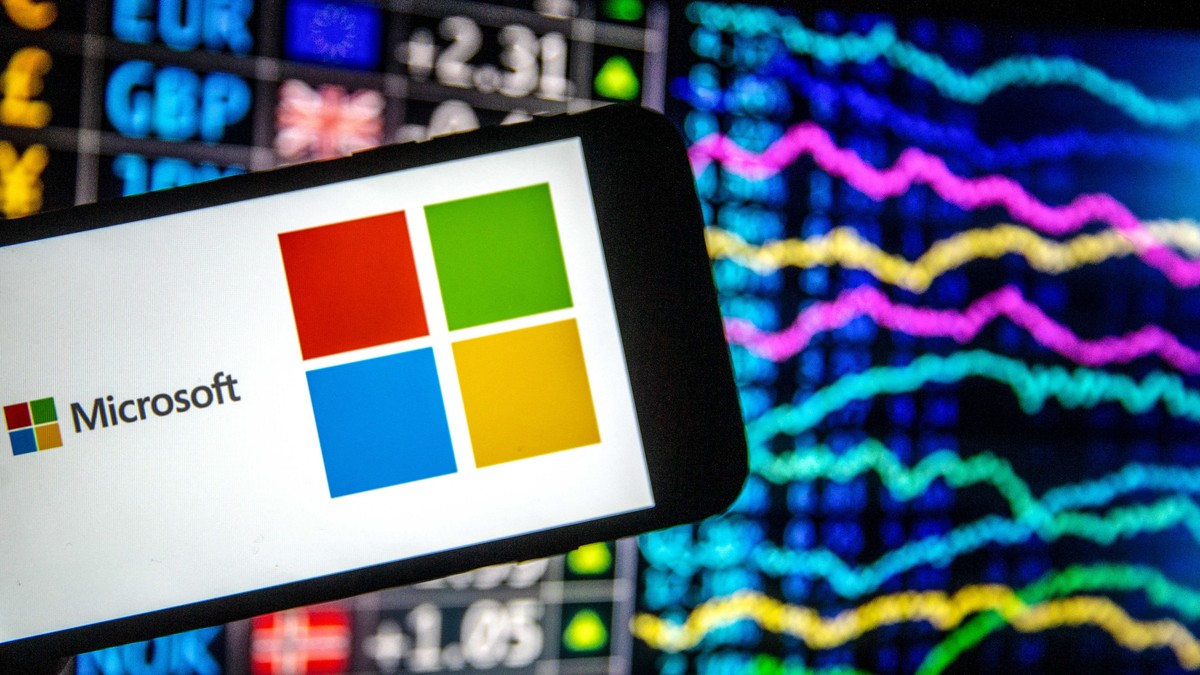 Windows 11, aproape de lansare. Ce facilități va avea viitoarea versiune a sistemului de operare. Smartphone cu logo-ul Windows și numele Microsoft pe el, având în spate grafice bursiere