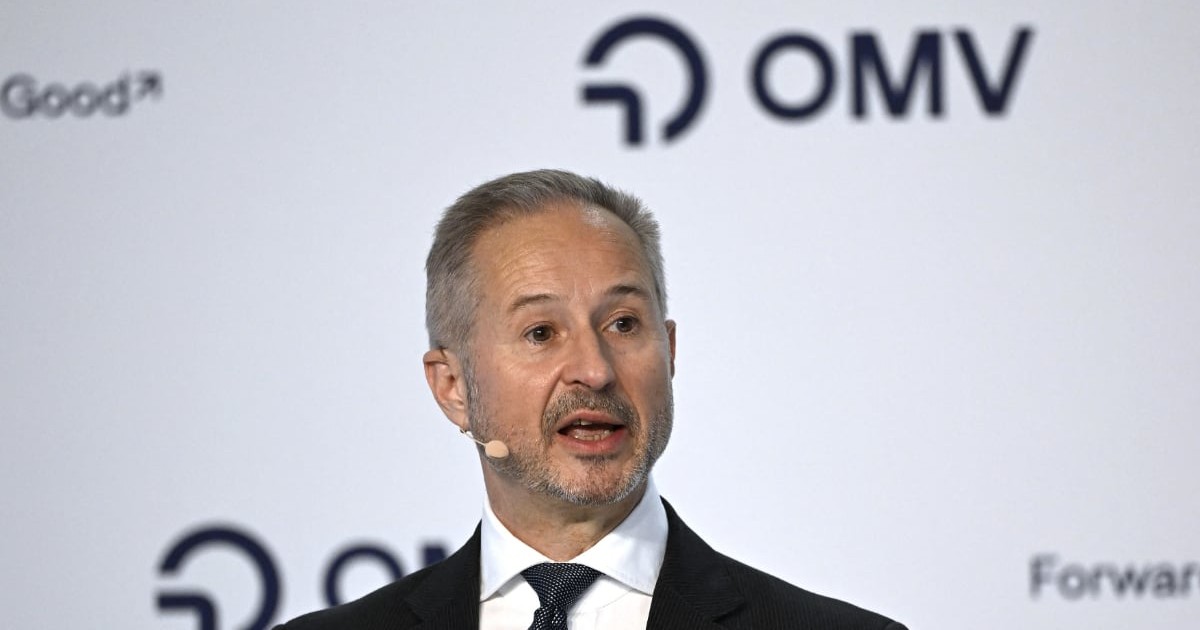 Un bărbat îmbrăcat în costum și cravată vorbește la un eveniment public, având un microfon prins la ureche. În fundal se vede logo-ul companiei OMV, sugerând că discursul are loc în cadrul unei conferințe sau prezentări organizate de companie.
