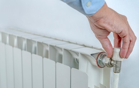 Mâna unui bărbat care reglează butonul caloriferului sistemului de încălzire pentru a economisi energie.