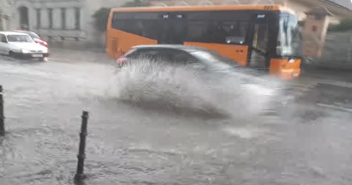 Cod galben de vreme instabilă în Sibiu și alte 8 judeţe. Mașină care trece pe lângă un autobuz portocaliu, printr-o baltă mare formată în urma unei averse