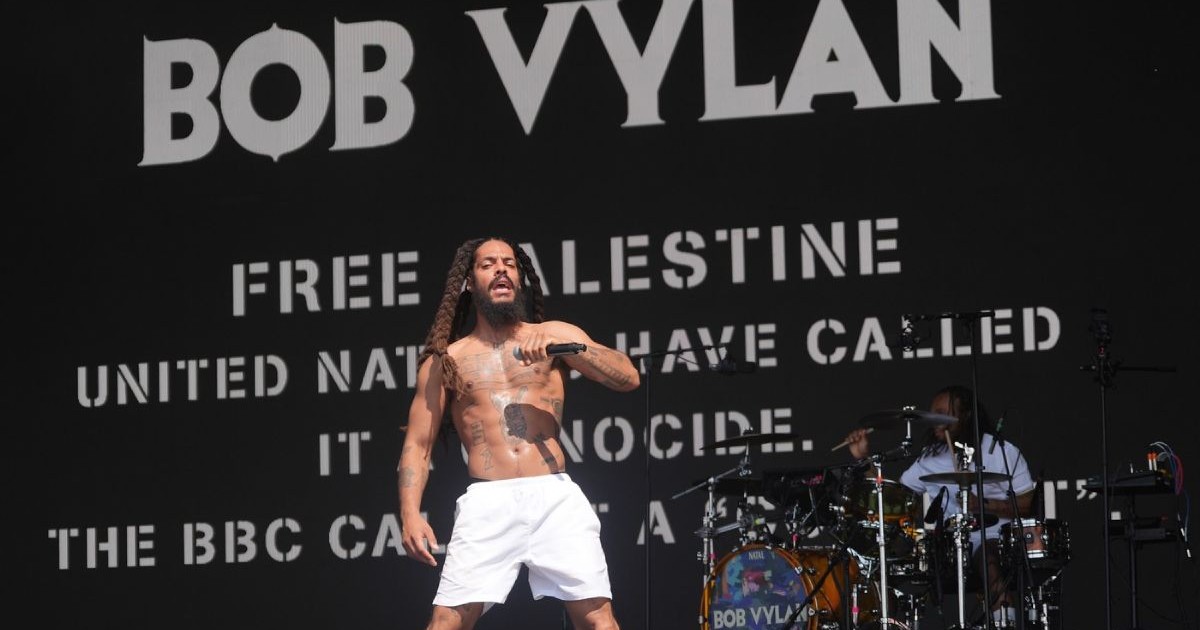 Bob Vylan, în bustul gol și șort alb, cântând pe scena West Holts, în timpul Festivalului Glastonbury de la Worthy Farm din Somerset, sâmbătă, 28 iunie 2025.