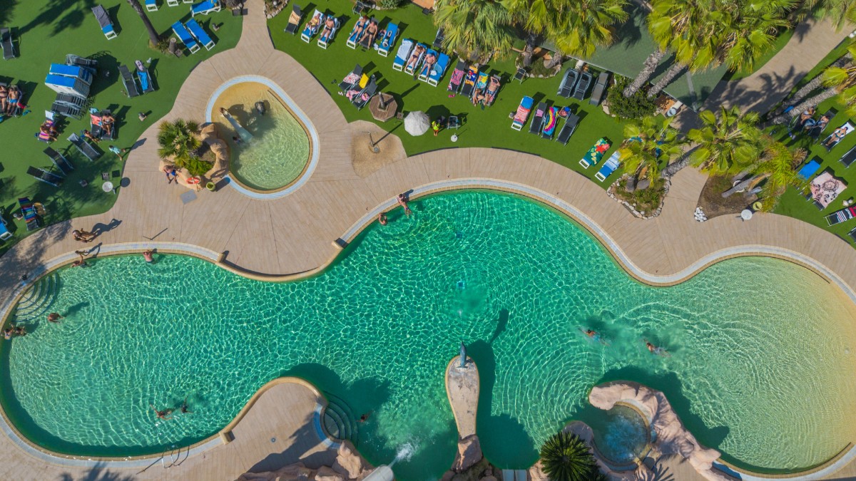 Piscina unui hotel din Spania, înconjurată de șezlonguri su salteluțe albastre și palmieri