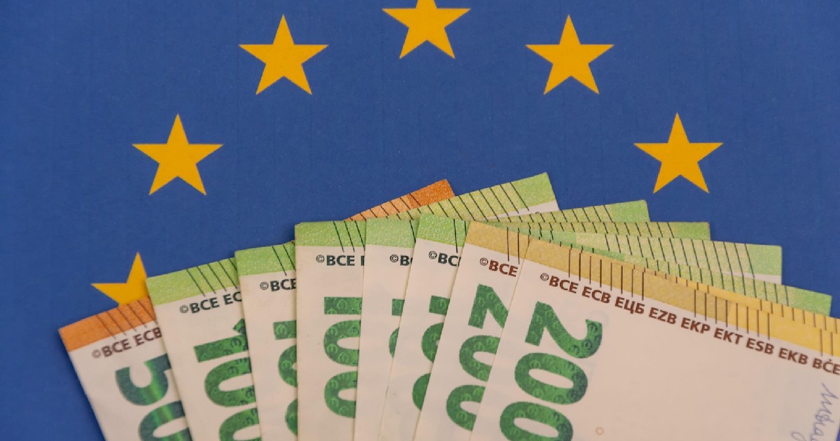 Un teanc de bancnote euro este așezat pe fundalul drapelului Uniunii Europene.