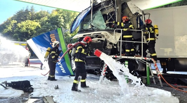 Pompieri în echipament de protecție acționând cu spumă de stingere la locul accidentului în care cabina unui camion a fost distrusă în urma impactului cu structura unei benzinării.