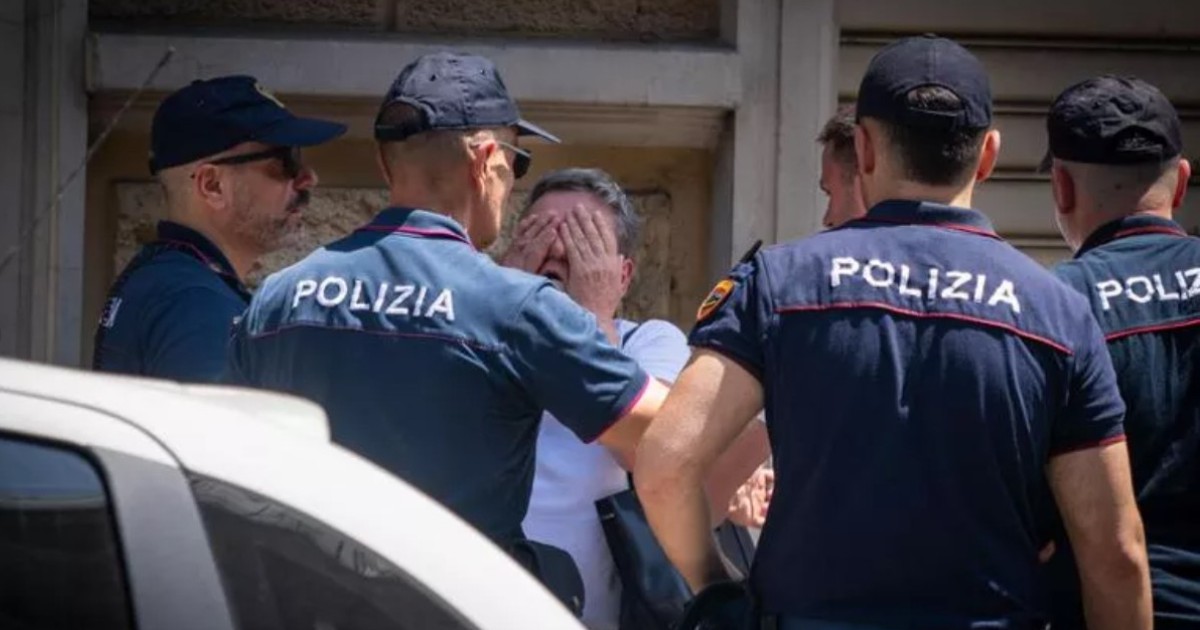 Un grup de polițiști italieni în uniforme, adunați în jurul unei persoane care își acoperă fața cu ambele mâini într-un gest de disperare sau suferință.