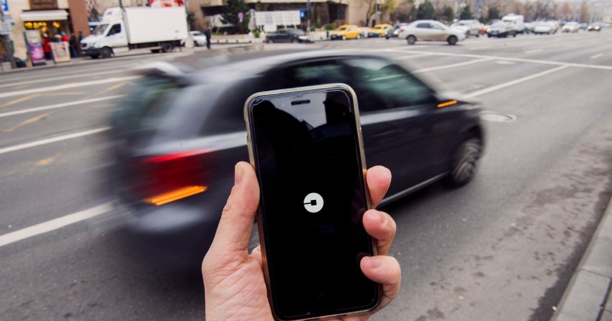 Bărbat care ține un smartphone cu aplicația Uber deschisă și așteaptă o mașină, în București.