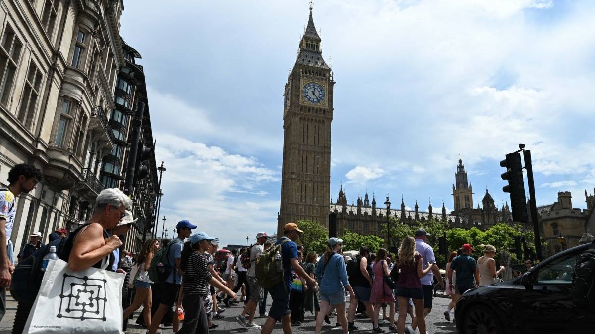 Un grup de trecători traversează strada în Londra, în fața Big Ben, într-o zi caniculată, oamenii sunt îmbrăcați subțire și se protejează de căldură cu șepci