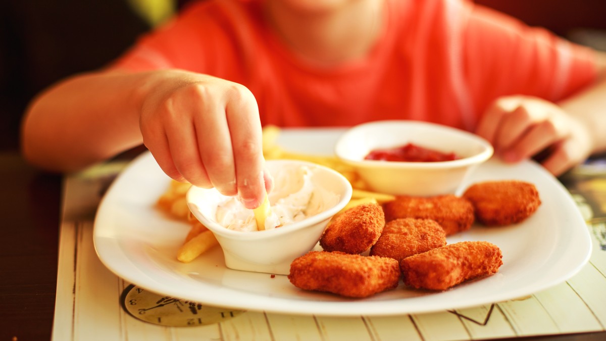 copil aflat la masa care mananca nuggets