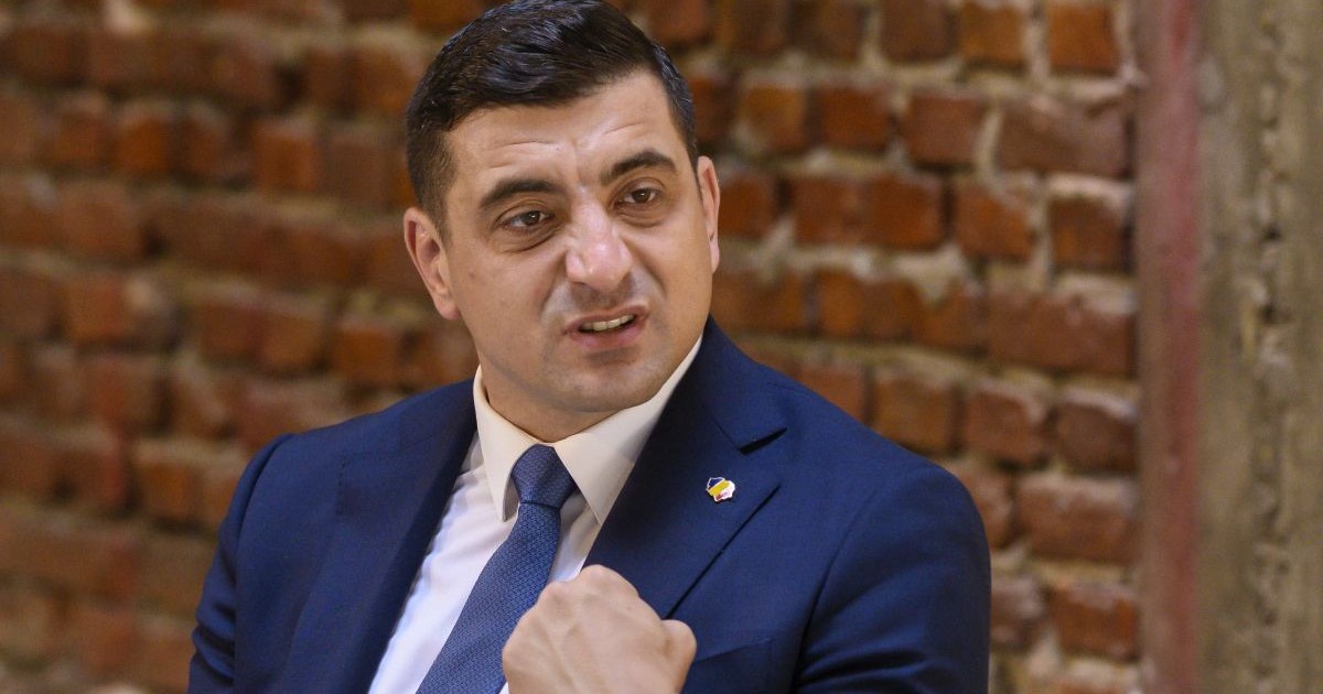 George Simion, îmbrăcat într-un costum de culoare albastră, având în spate un perete de cărămidă