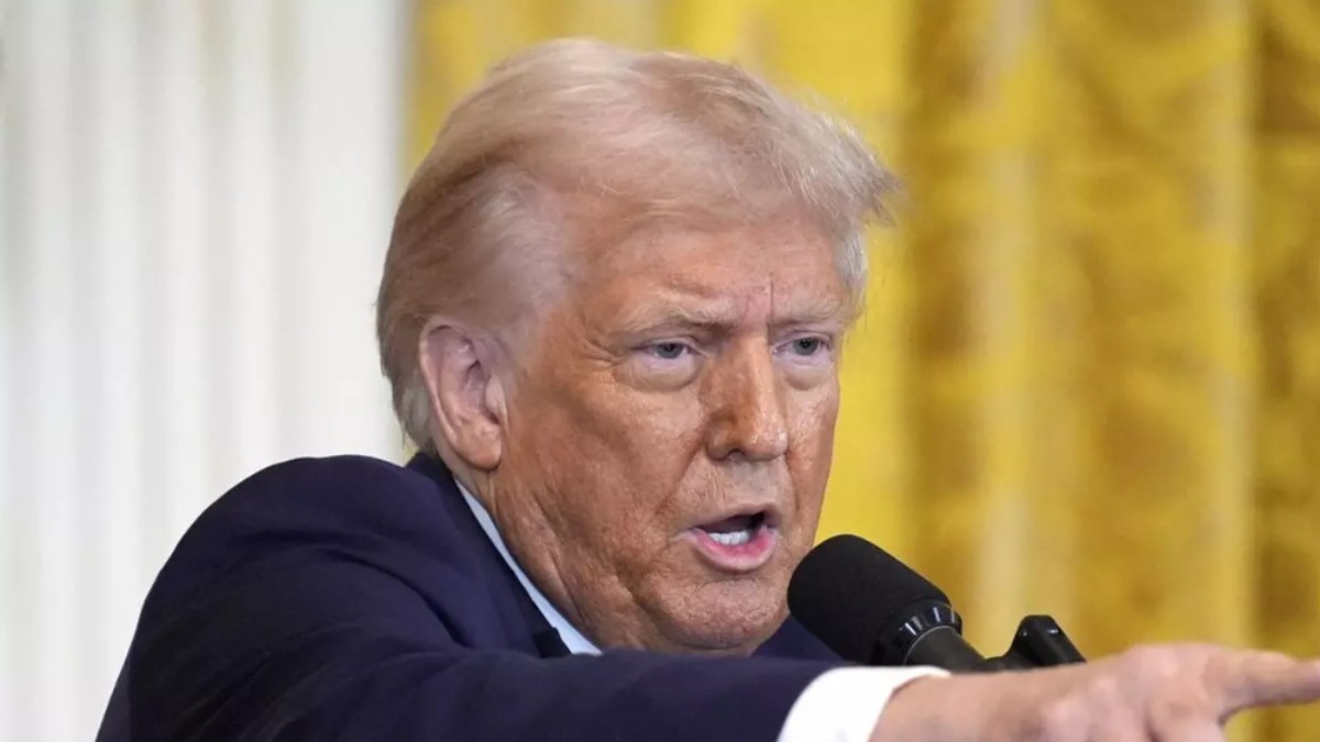 În imagine este ilustrat Donald Trump, îmbrăcat în costum negru și cămașă albă. Acesta vorbește la microfon