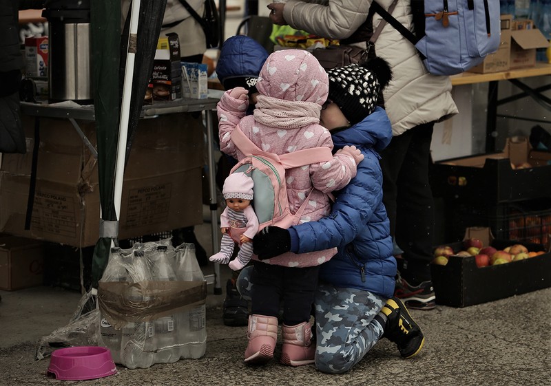Un băieţel încearcă să-şi încălzească sora, în timp ce mama lor primeşte mâncare şi băuturi fierbinţi de la voluntari