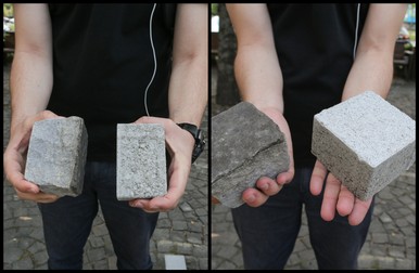 În mâna stângă, piatra cubică ce urmează să fie înlocuită cu un fel de „piatră” cubică din beton, prezentată în mâna dreaptă