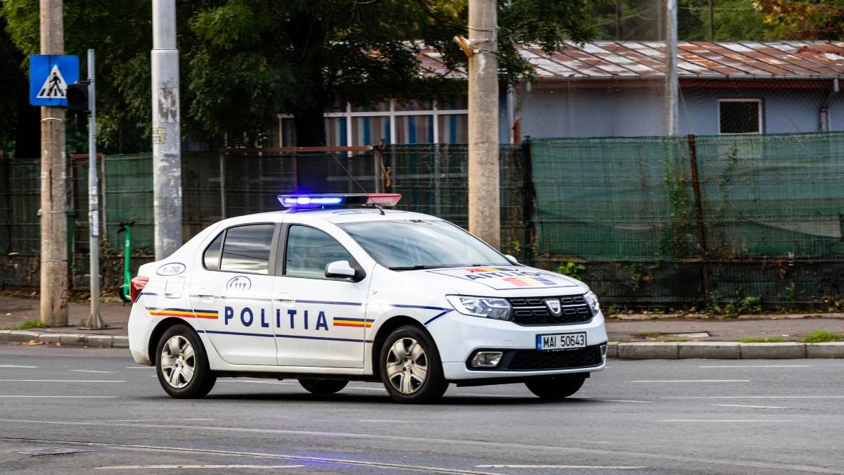 O mașină de poliție mergând pe stradă ziua în oraș cu girofarul pornit