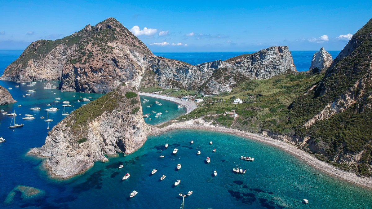 Panoramă deasupr Insulei Parmalora din Italia, în apă se văd zeci de bărci ale turiștilor, insula este formată din munți stâncoși acoperiți de vegetație