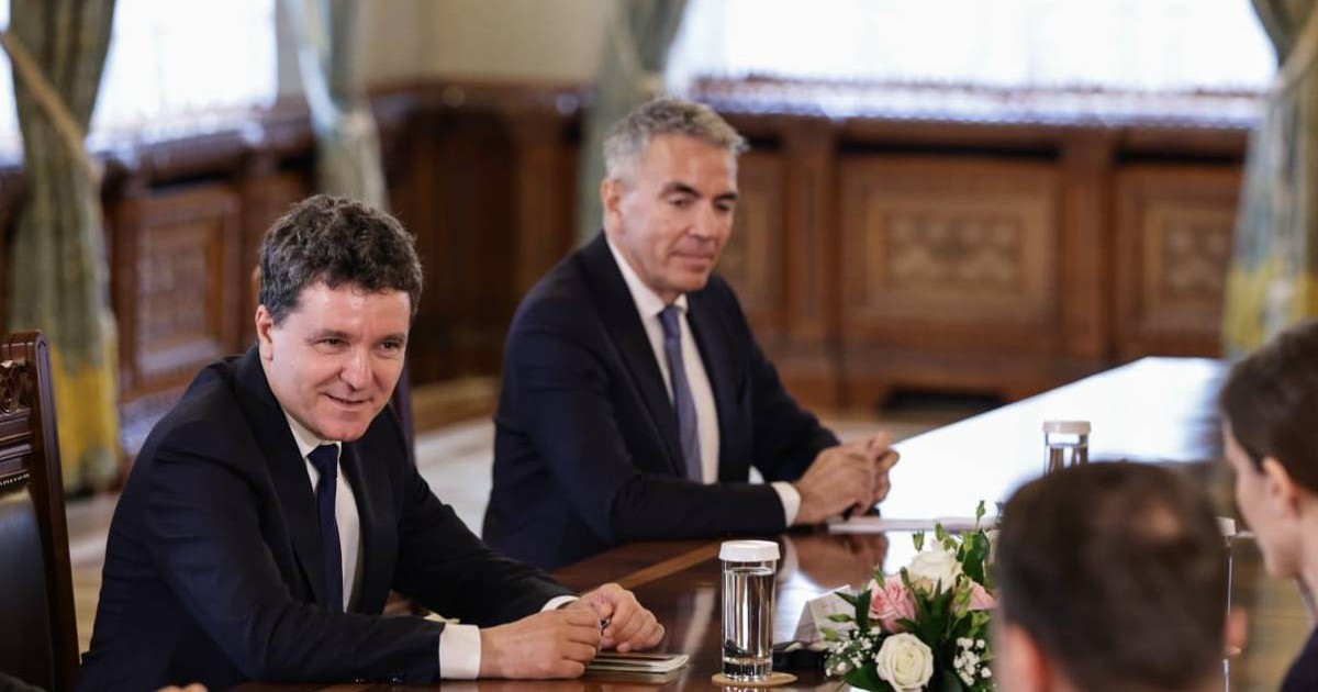 Președintele Nicușor Dan, în timpul negocierilor de joi de la Palatul Cotroceni, stă la masa cu alți politicieni români, îmbrăcat la costum și zâmbește