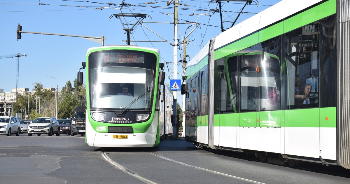 Imaginea, realizată într-o zi senină și luminoasă, surprinde două tramvaie moderne vopsite în alb și verde, care circulă pe șine paralele pe o stradă din oraș. În plan central, tramvaiul din stânga este marcat cu destinația "Piața Presei, Ghencea" (indicând probabil Bucureștiul) și are în fundal mașini la o intersecție.