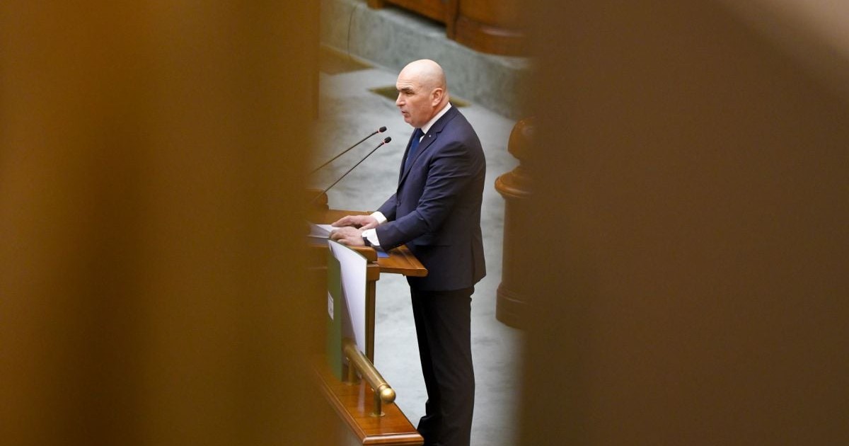 Ilie Bolojan, în picioare, îmbrăcat în costum albastru închis, la pupitrul din Parlamentul României, pe 9 februarie 2026