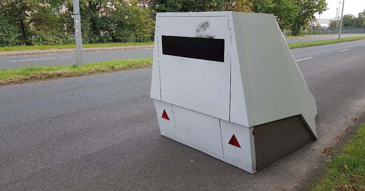 Imaginea prezintă un radar de viteză alb, dreptunghiular, amplasat pe o stradă