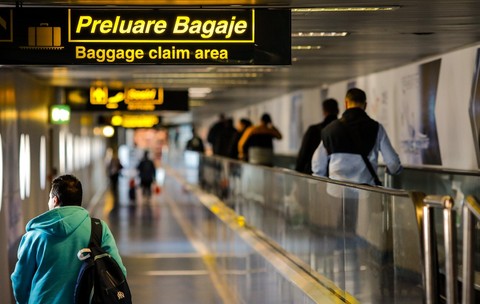 Imaginea surprinde culoarul de acces către zona de preluare a bagajelor dintr-un aeroport, semnalizată printr-un panou luminos cu inscripția „Preluare Bagaje / Baggage claim area”. Foto: Shutterstock